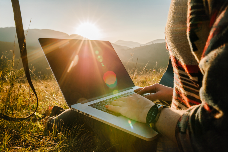 image of a person sitting outside on a field with their laptop. 